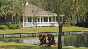 A house with a porch, a pond, and two Adirondack chairs.