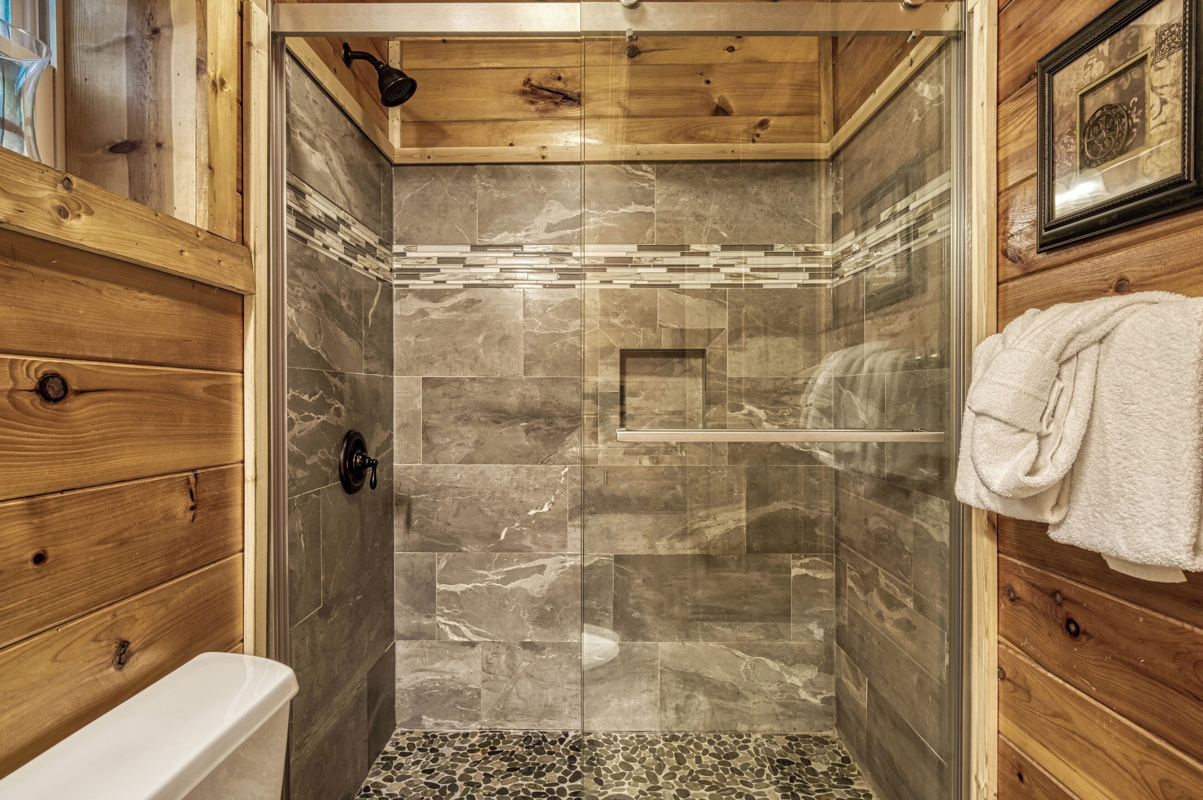A shower with a glass door, wooden walls, and a tiled floor.