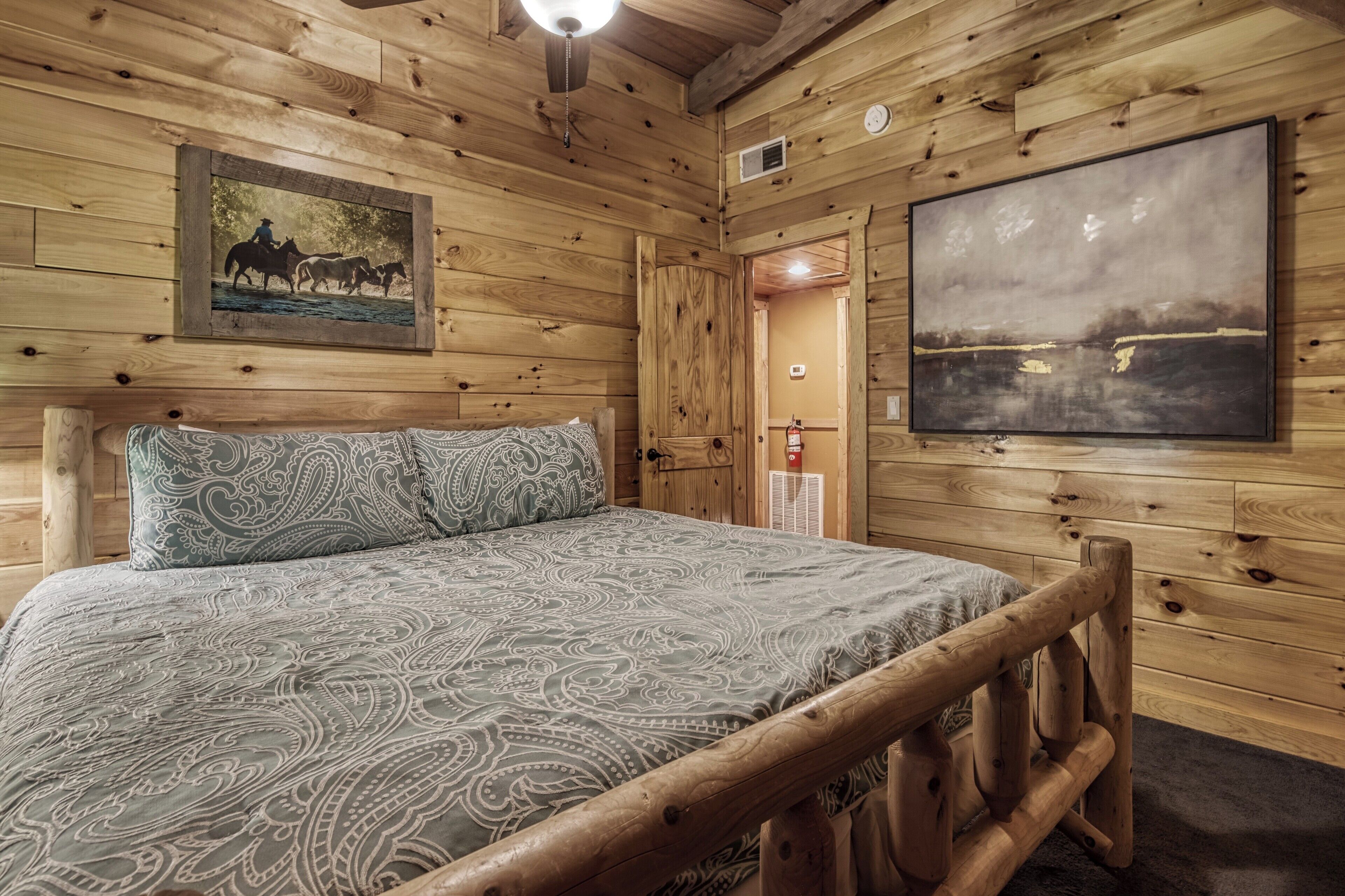 Una habitación tipo cabaña de madera con una cama, un cuadro colgado y un ventanal grande.