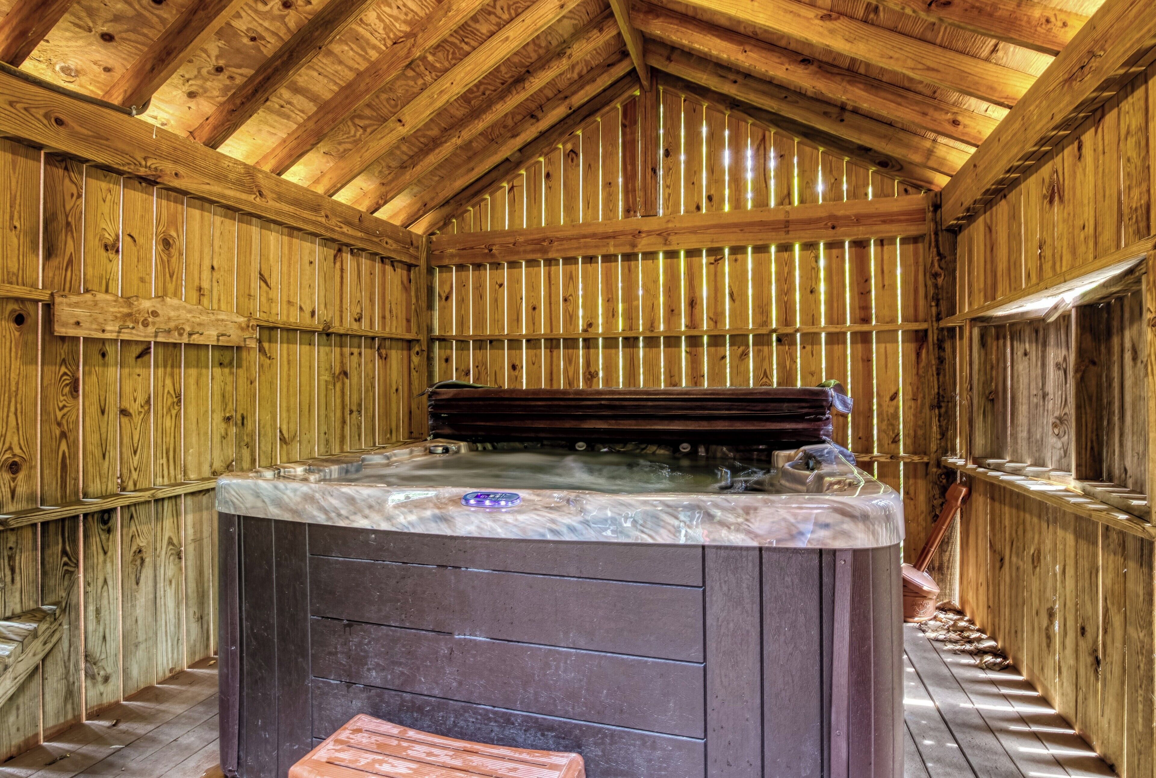 A wooden spa room with a hot tub, wooden walls, and a sloped ceiling.