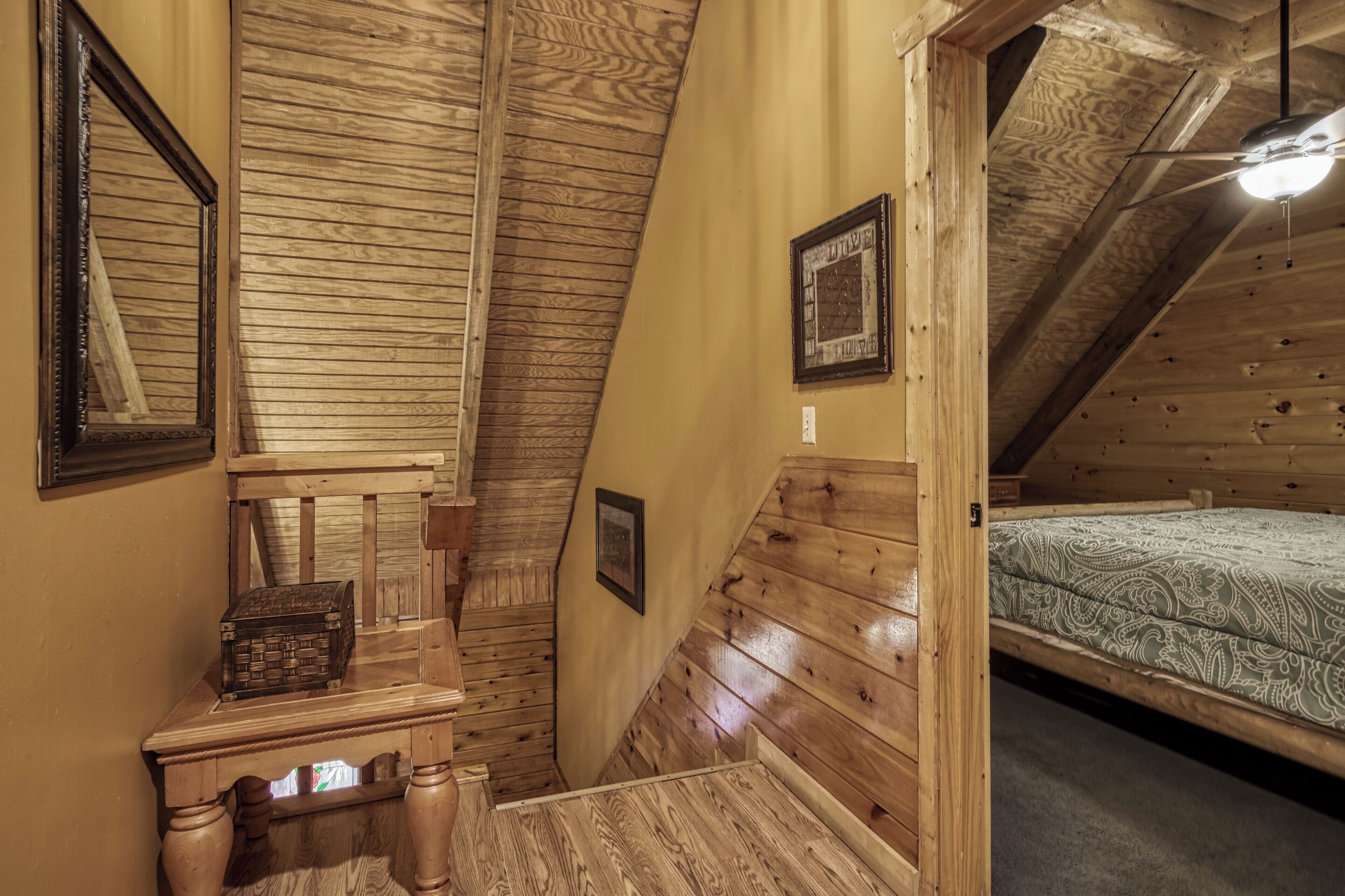 A wooden attic bedroom with a sloped ceiling, a bed, a chest of drawers, and a small table.