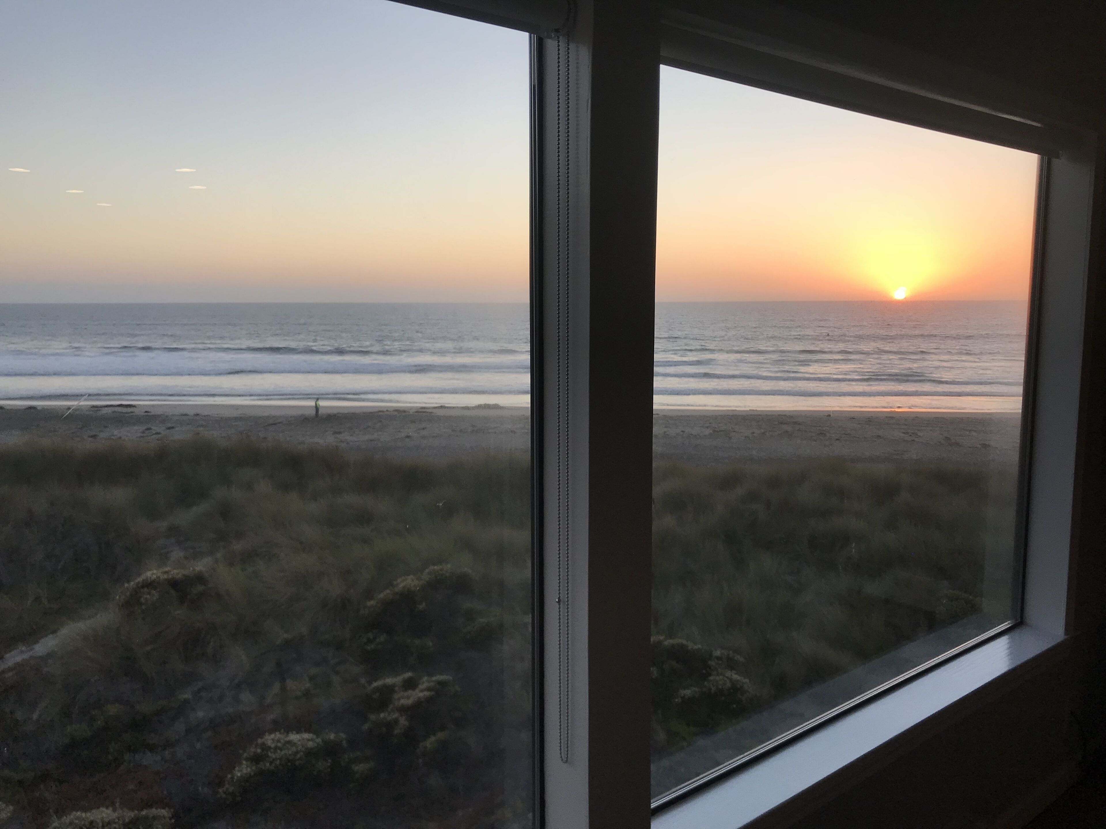 Vista del océano a través de una ventana, con el sol poniéndose en el horizonte.
