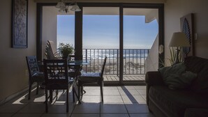 Un balcon avec vue sur la plage, un coin repas avec des chaises et une table, et un canapé.