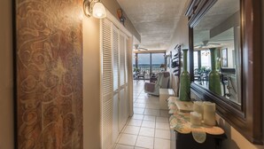 Un couloir avec un mur décoré de motifs, une vue sur l’océan et un coin salon avec une table et des chaises.