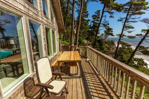 A wooden deck with a table and chairs, overlooking a beach and forested area.