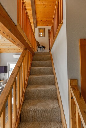 A wooden staircase with carpeted steps leading to a room with a chair and a television. - Honeymoon Cove- Exclusive Beach, Ocean View & Spa (Gold Beach)