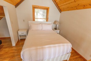 Een slaapkamer met een groot bed, houten balken in het plafond, een raam en een nachtkastje met een lamp.