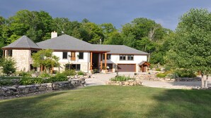 A two-story house with a stone facade, a grey roof, and a well-maintained lawn.
