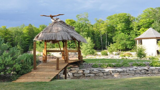 A wooden gazebo with a thatched roof and a stone pathway leading to it.