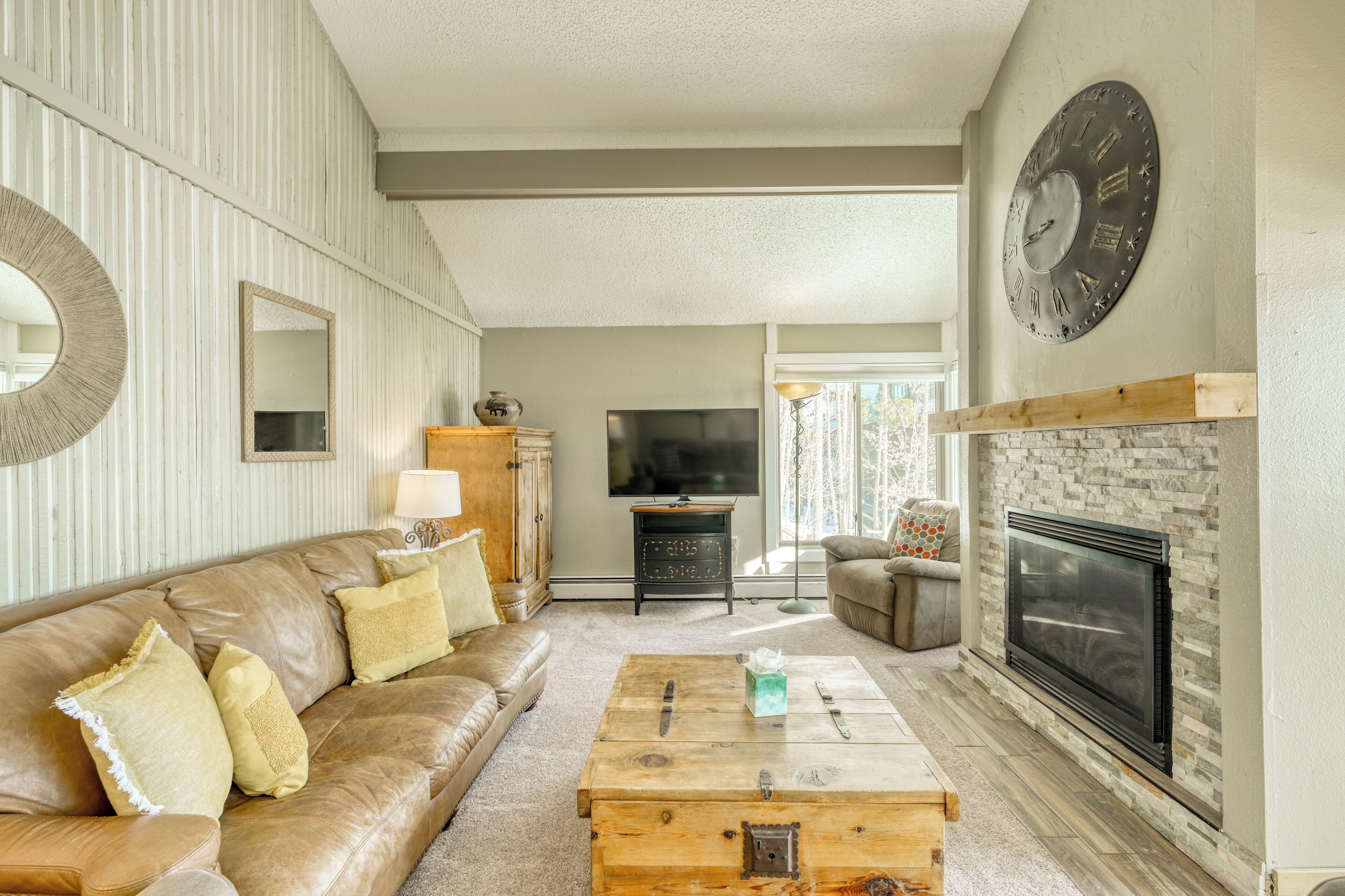 A living room with a leather sofa, a wooden coffee table, a fireplace, and a large wall clock.