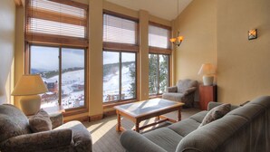 Una sala de estar acogedora con ventanas amplias, un sofá, una mesa de centro y lámparas.