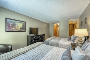 A hotel room with two beds, a desk, a chair, a dresser, a television, and a painting on the wall.