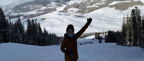 A person skiing on a snowy slope with mountains in the background.