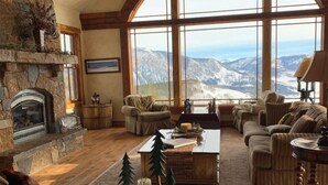 A cozy living room with a stone fireplace, large windows offering a mountain view, and comfortable seating. - 5250 Sq Ft. 5-Star Mountain Home with 360° Peak & Valley Views (Crested Butte)