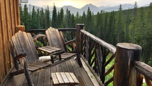 A wooden deck with chairs and a table, overlooking a forest and mountains. - 5250 Sq Ft. 5-Star Mountain Home with 360° Peak & Valley Views (Crested Butte)