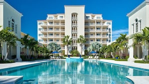 A hotel with a central swimming pool, surrounded by palm trees and lounge chairs.
