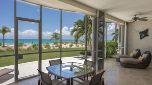A spacious room with a glass table and chairs, a sofa, and a view of the beach and ocean.
