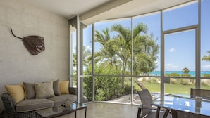 A spacious living area with a large glass wall offering a view of palm trees and the ocean.