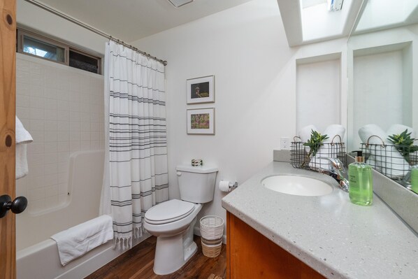 Une salle de bain avec une baignoire, des toilettes et un lavabo. Deux tableaux encadrés sont accrochés au mur.