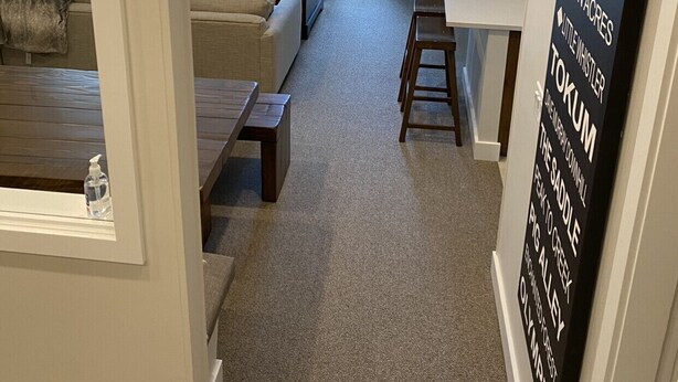 Un salon moderne avec un canapé, une table basse et une cheminée. Une grande fenêtre offre une vue sur les arbres. Un panneau sur le mur indique les marques de whisky disponibles.