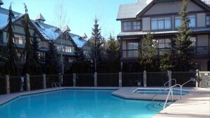 Une piscine dotée d’une terrasse en bois, entourée d’une clôture et d’arbres.