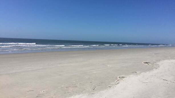 Une vaste plage de sable fin, avec des vagues douces et un ciel bleu dégagé.