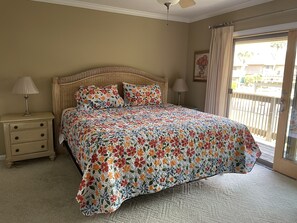 A bedroom with a large bed, a nightstand with a lamp, a window with curtains, and a view of the outside.