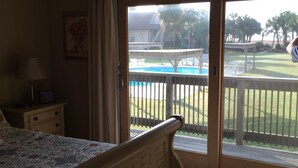 Une chambre avec un lit, une table de chevet, une lampe et une vue sur une piscine et un espace extérieur, accessible par une porte-fenêtre coulissante.