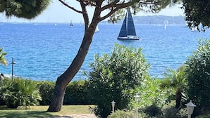 A paved pathway leading to a scenic view of the sea with sailboats, surrounded by lush greenery and trees. - Premium Beachfront Villa, Panoramic View of St Tropez Bay (Sainte-Maxime)