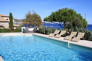 A swimming pool with lounge chairs and a view of the sea.