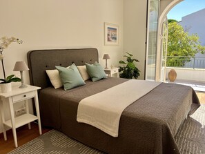 A bedroom with a bed, nightstands, a lamp, a potted plant, and a painting on the wall.