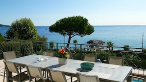 A table set outdoors with a view of the sea and a rocky outcrop. - Premium Beachfront Villa, Panoramic View of St Tropez Bay (Sainte-Maxime)