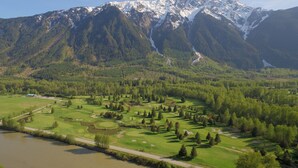 En golfbane med en flod i forgrunden og bjerge i baggrunden.