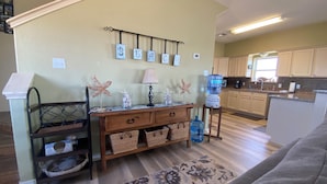 A living room with a wooden bench, a lamp, starfish decorations, a water dispenser, and a kitchen in the background. - Spacious 4 B/R 3 BA - best of both - Bay and Gulf  (Surfside)