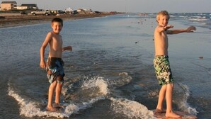 Two children on a beach with waves, a truck, and beachgoers in the background. - Spacious 4 B/R 3 BA - best of both - Bay and Gulf  (Surfside)