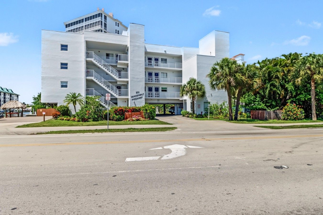A multi-story hotel with a central staircase, a parking lot, and lush landscaping.