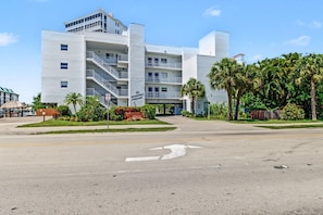 A multi-story hotel with a central staircase, a parking lot, and lush landscaping.