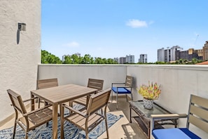 A rooftop terrace with a table and chairs, a potted plant, and a view of city buildings.