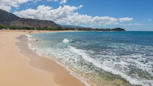 A beach with clear blue water, sandy shore, and mountains in the background.
