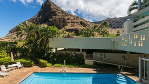 A swimming pool with a view of a mountain, palm trees, and a building with balconies.