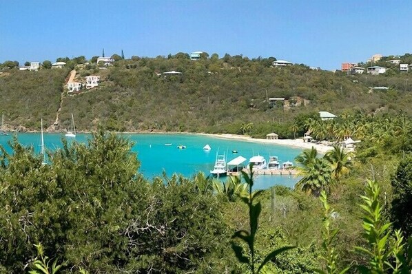 A coastal view with boats docked near a beach, surrounded by greenery and buildings on a hillside.