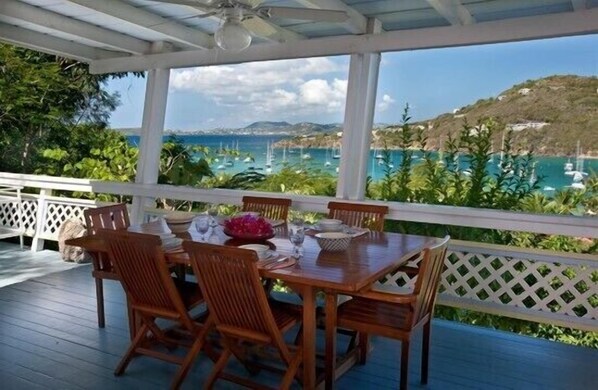 A covered outdoor dining area with a wooden table and chairs, overlooking a coastal view with boats and greenery. - Idyllic Villa - Great Pool and deck areas, great family home, A/C throughout (Cruz Bay)