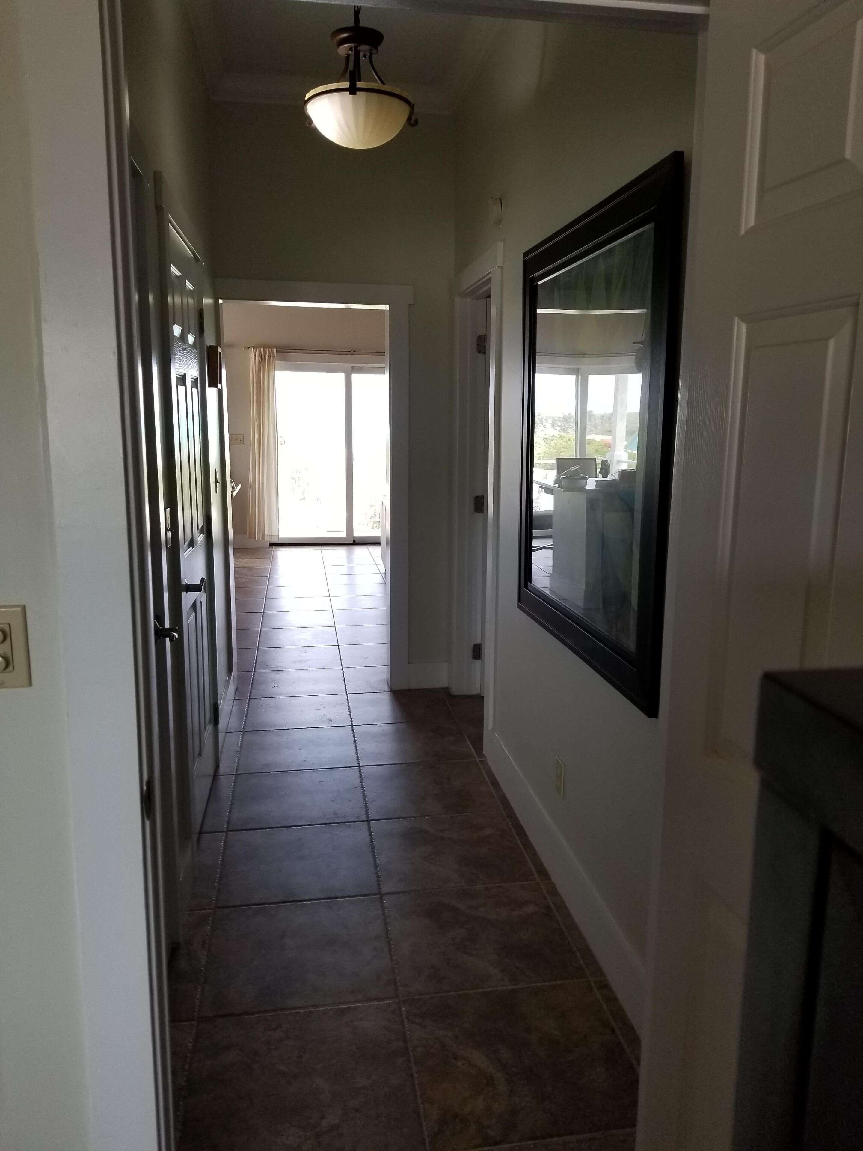 A hallway with a tiled floor, a ceiling light fixture, and a door with a window.