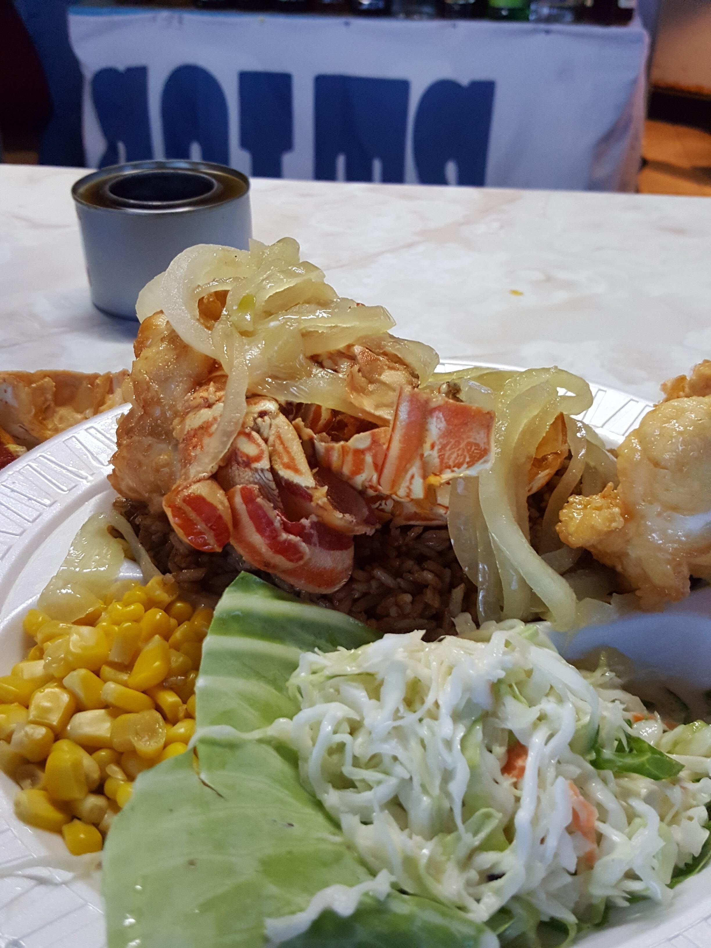 Uma refeição com lagosta, milho e salada de couve num prato branco.