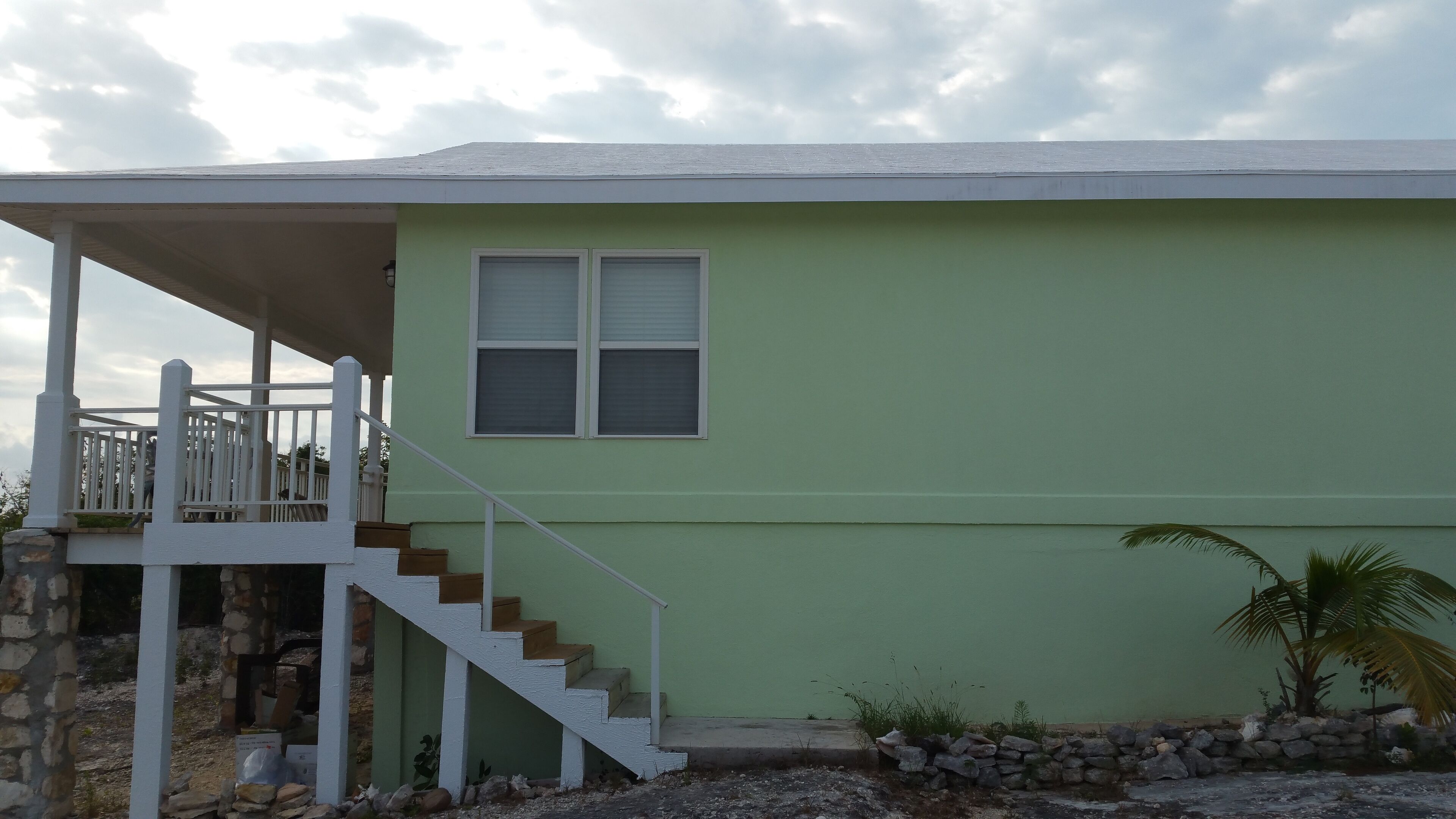 A two-story house with a porch, a staircase, and a small garden area with a palm tree.