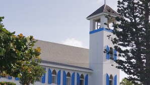 Um edifício branco com detalhes azuis, uma torre de sino e um jardim bem cuidado.