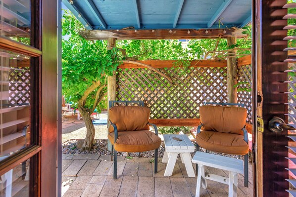 Un espace extérieur aménagé avec deux fauteuils marron à coussins et une petite table blanche, placé sous une pergola en bois avec un treillage en arrière-plan.