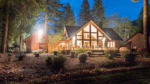 A large, two-story log cabin with a prominent front porch and large windows, surrounded by a forested landscape. - Mountain Golf Course Retreat (Mt Hood Village)