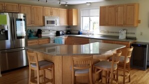 A kitchen with wooden cabinets, a stainless steel refrigerator, a microwave, a stove, and a dishwasher. There is a large island with bar stools.