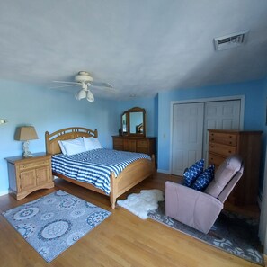 A bedroom with a wooden bed, a nightstand, a dresser, a chair, a mirror, and a ceiling fan. - Newly Refreshed! Prime Location - Walk to Nrgst Pier Beach or Narrow River. (Narragansett)